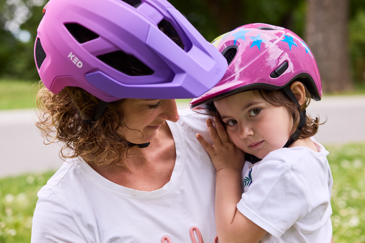 Mutter und Kind mit pinken KED Kinderhelmen auf einer Wiese